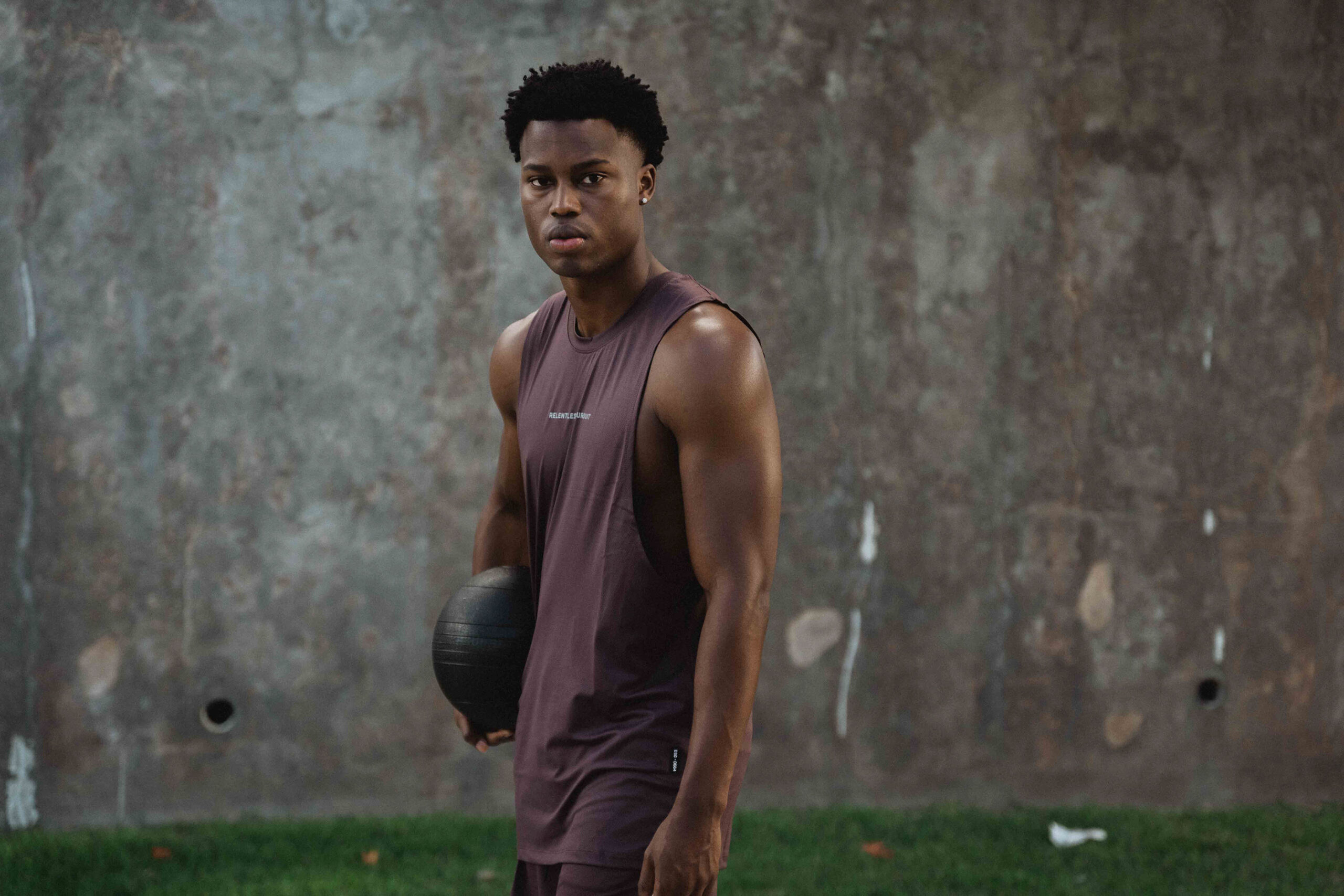 Black male fitness model posing for ASRV in front of a concrete wall