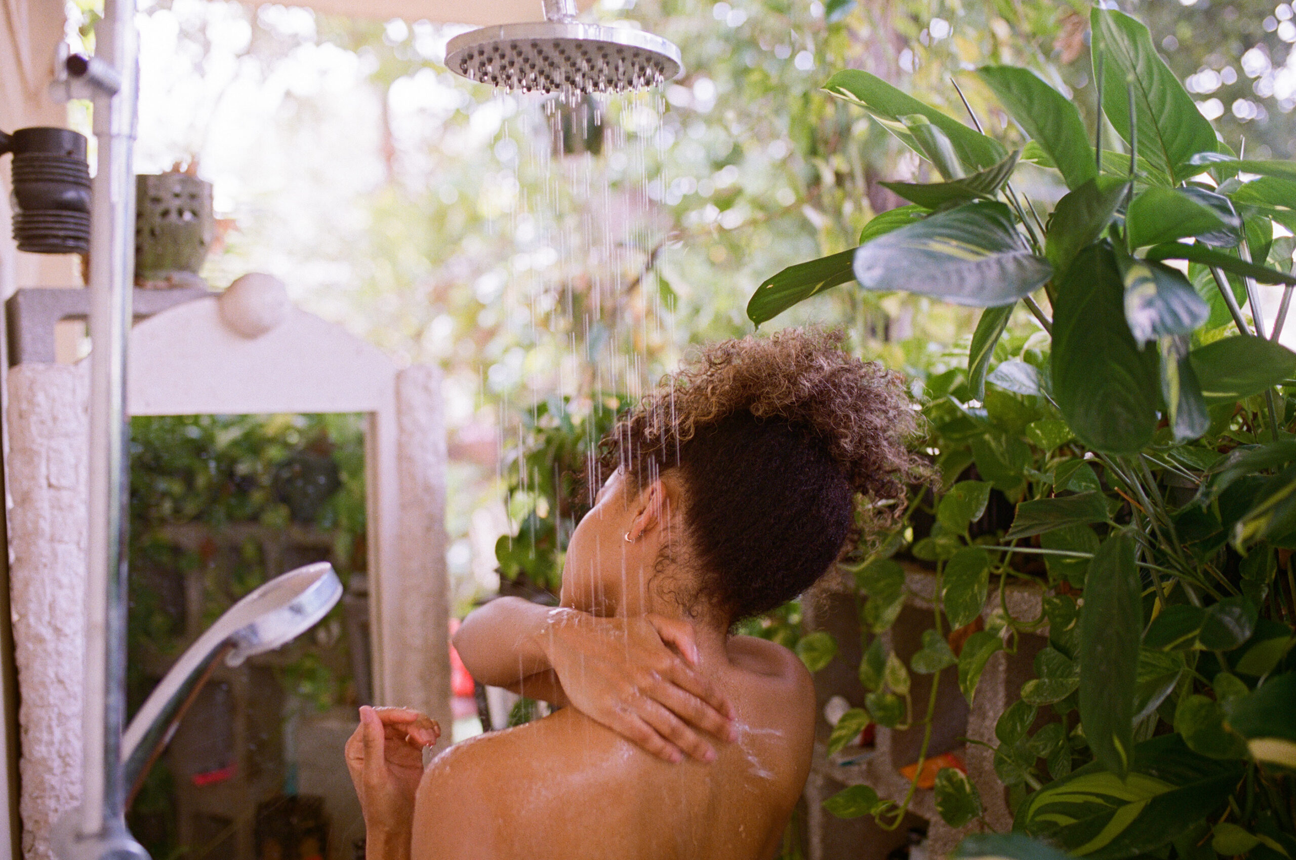 Female model showering outdoors in a very tropical location with a rain shower head