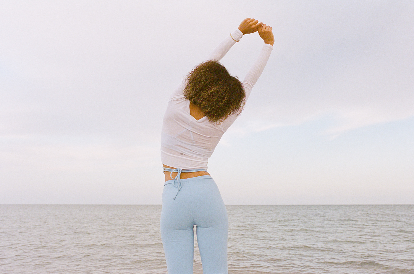 Female model wearing light blue Alo yoga leggings stretching in front of Miami ocean